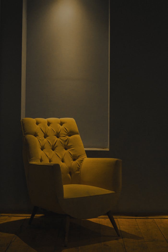 A stylish yellow chair in a dimly lit minimalist room creates a cozy ambiance.