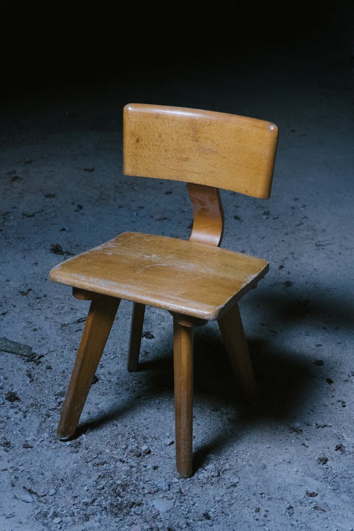A single vintage wooden chair is placed in a dimly lit indoor setting with a rustic atmosphere.