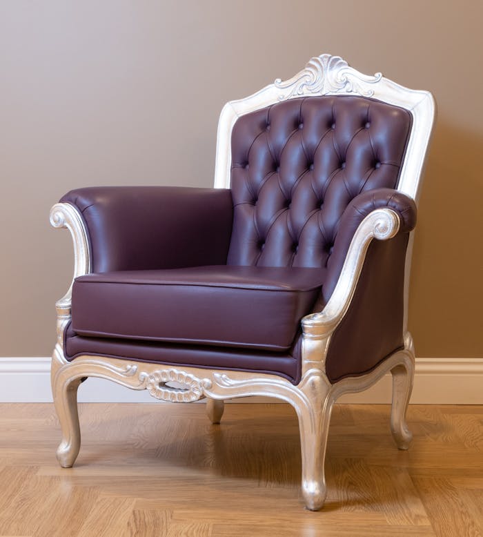 Luxurious leather armchair with tufted back and ornate frame on wooden floor.